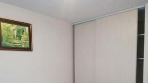 Et soveværelse med en seng, et natbord, en lampe, et klædeskab og et billede i ramme på væggen.