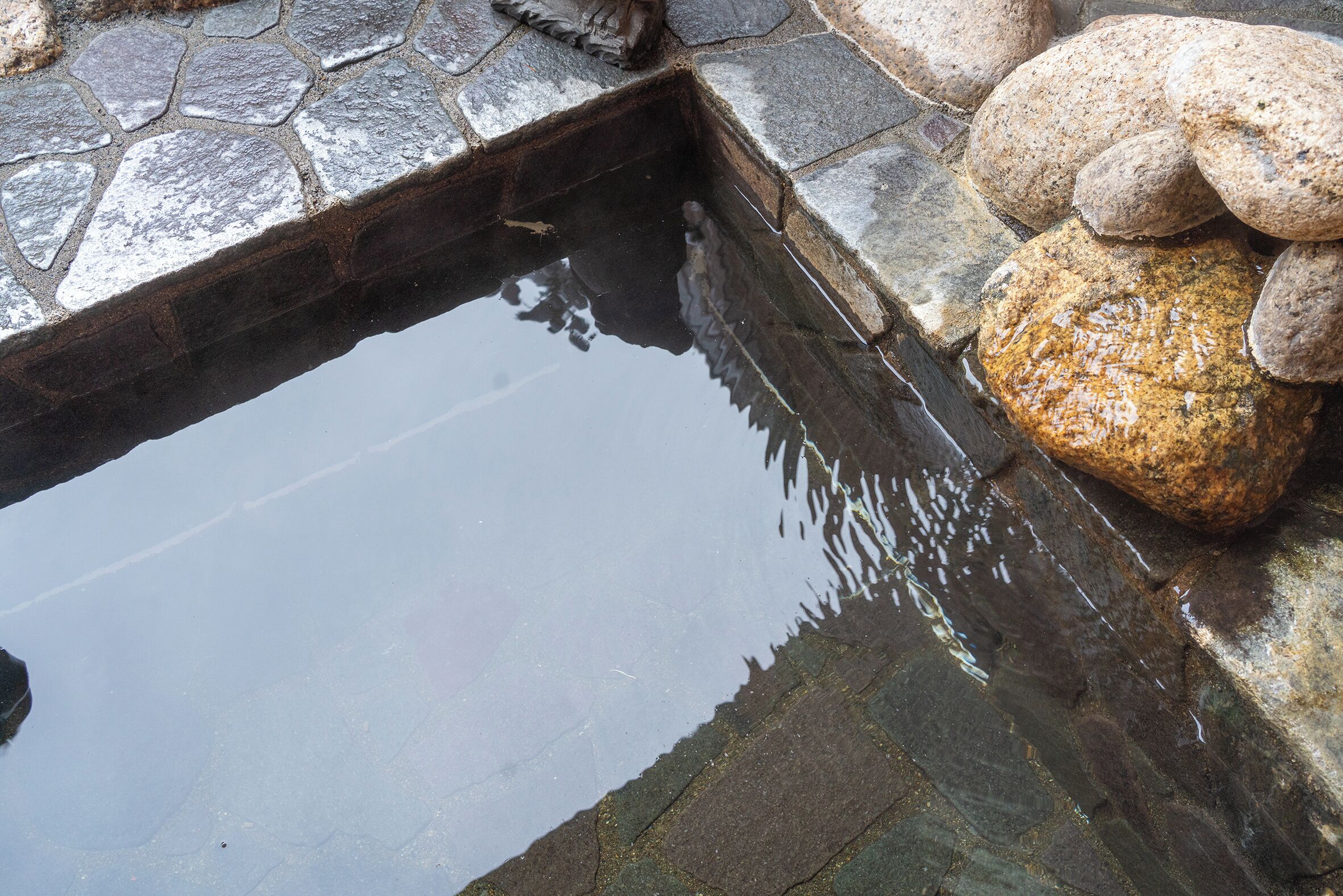 A stone-lined pond with clear water, surrounded by rocks and a stone edge.