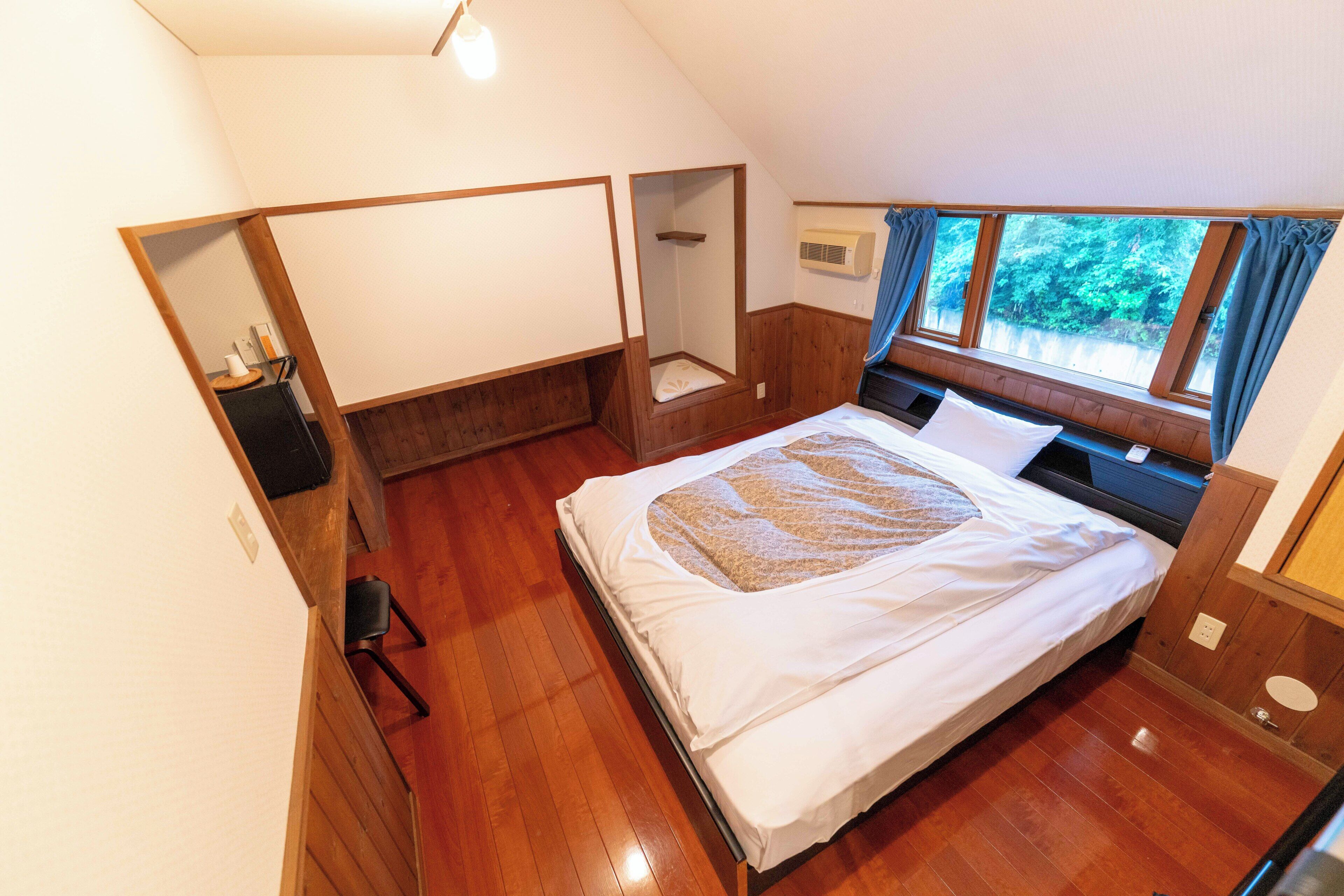 Una camera da letto con pavimento in legno, un letto con copriletto decorato, un comodino, una sedia e una finestra con vista sul verde.