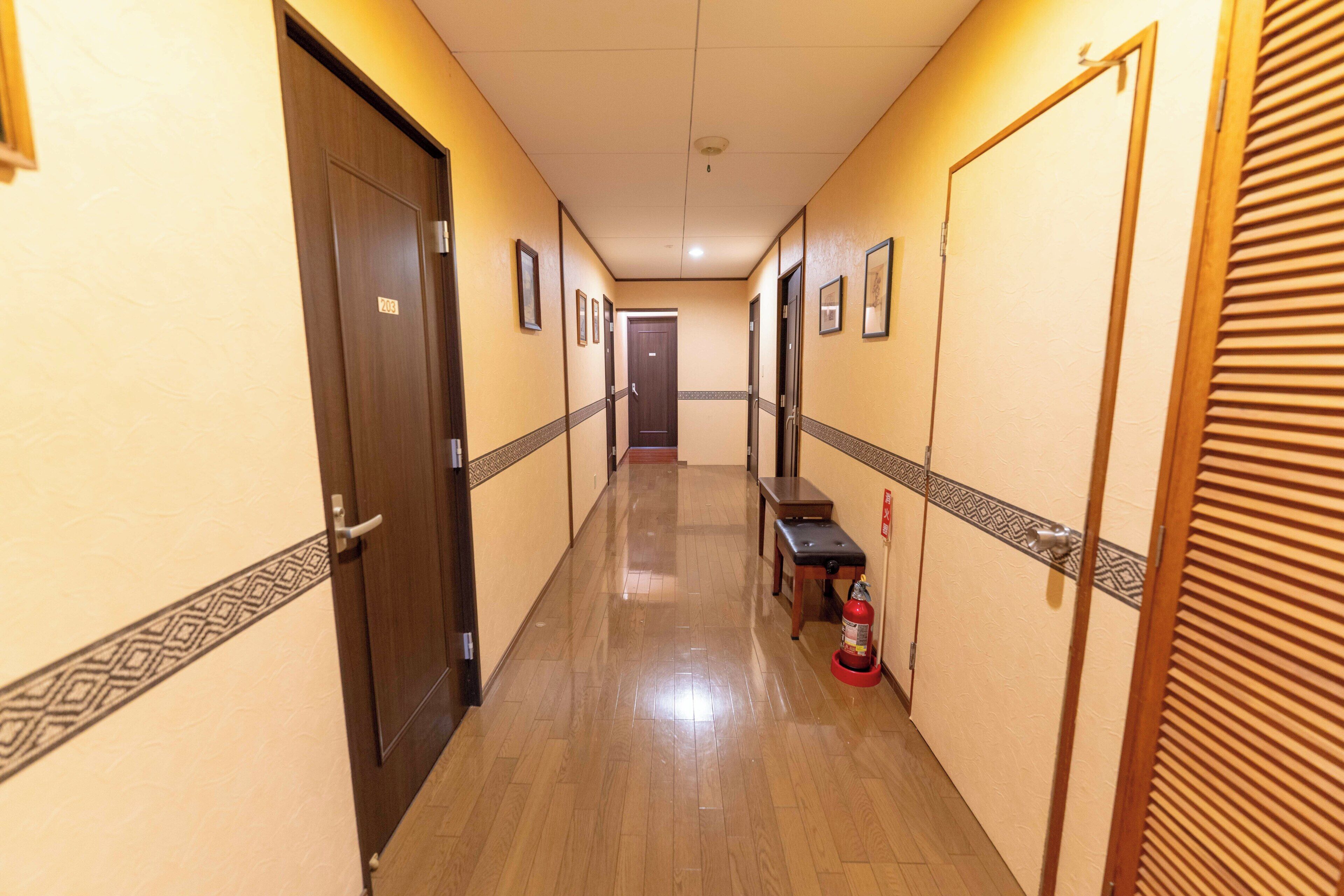 Un pasillo de hotel con puertas de madera, un banco y un extintor.