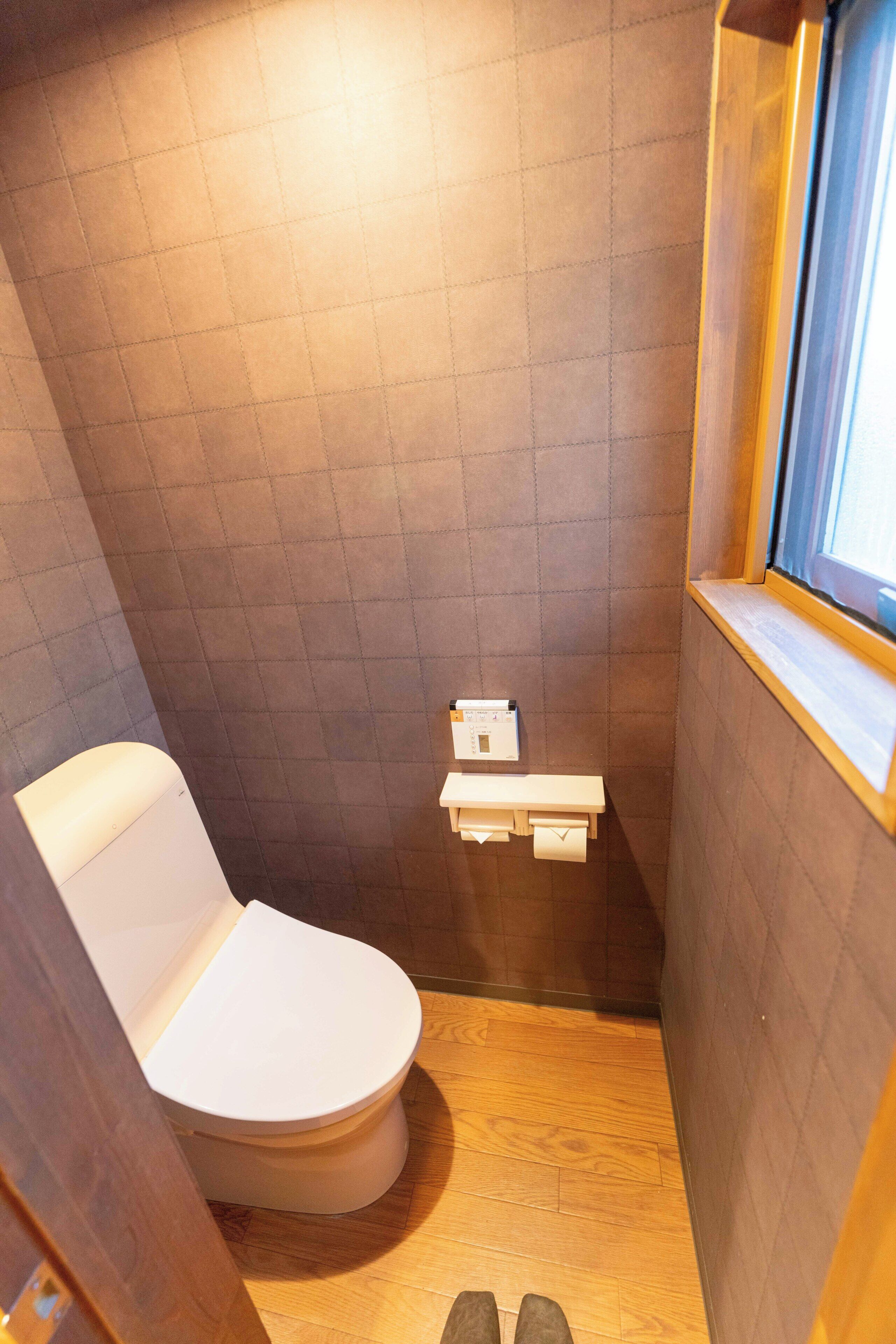 A compact bathroom with a toilet, a small shelf with a toilet paper holder, and a window.