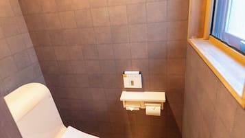 A compact bathroom with a toilet, a small shelf with a toilet paper holder, and a window.
