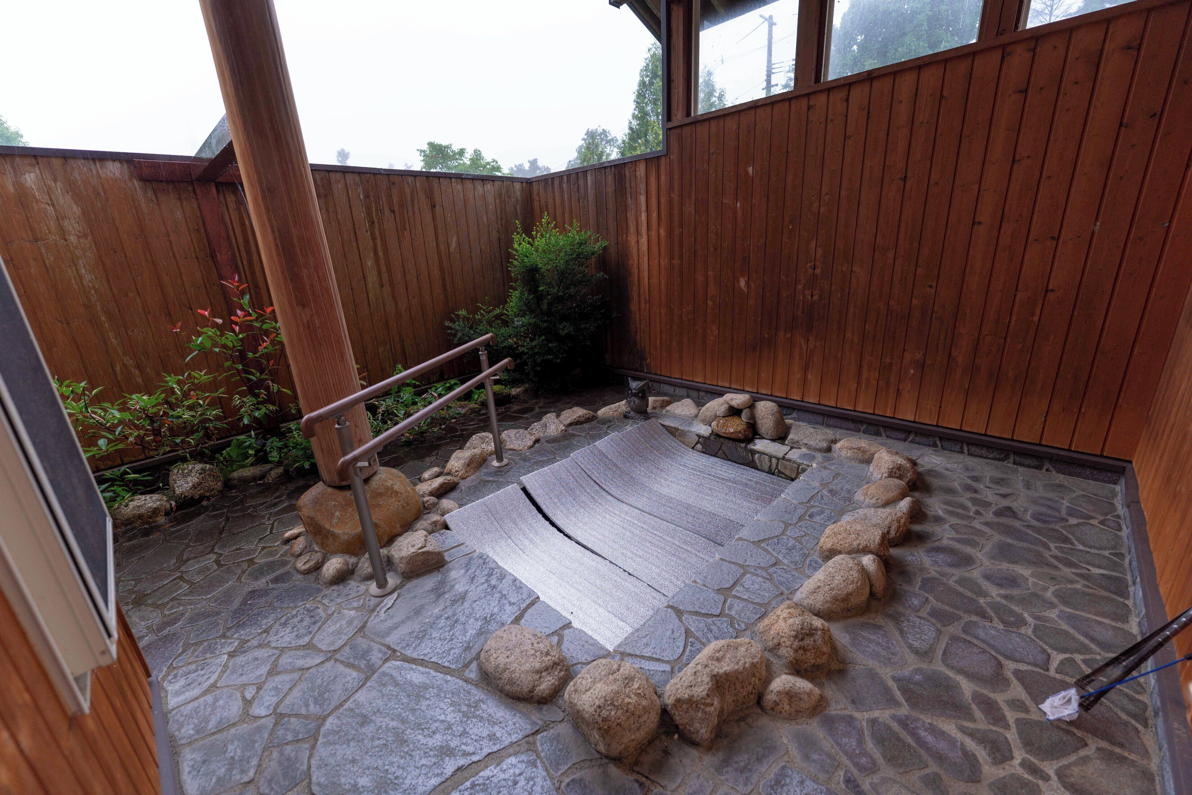 A stone patio with a wooden fence, a metal handrail, and a small garden area with rocks and plants.