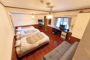 Habitación de hotel con dos camas, un escritorio con computadora, un sofá y una ventana con cortinas.