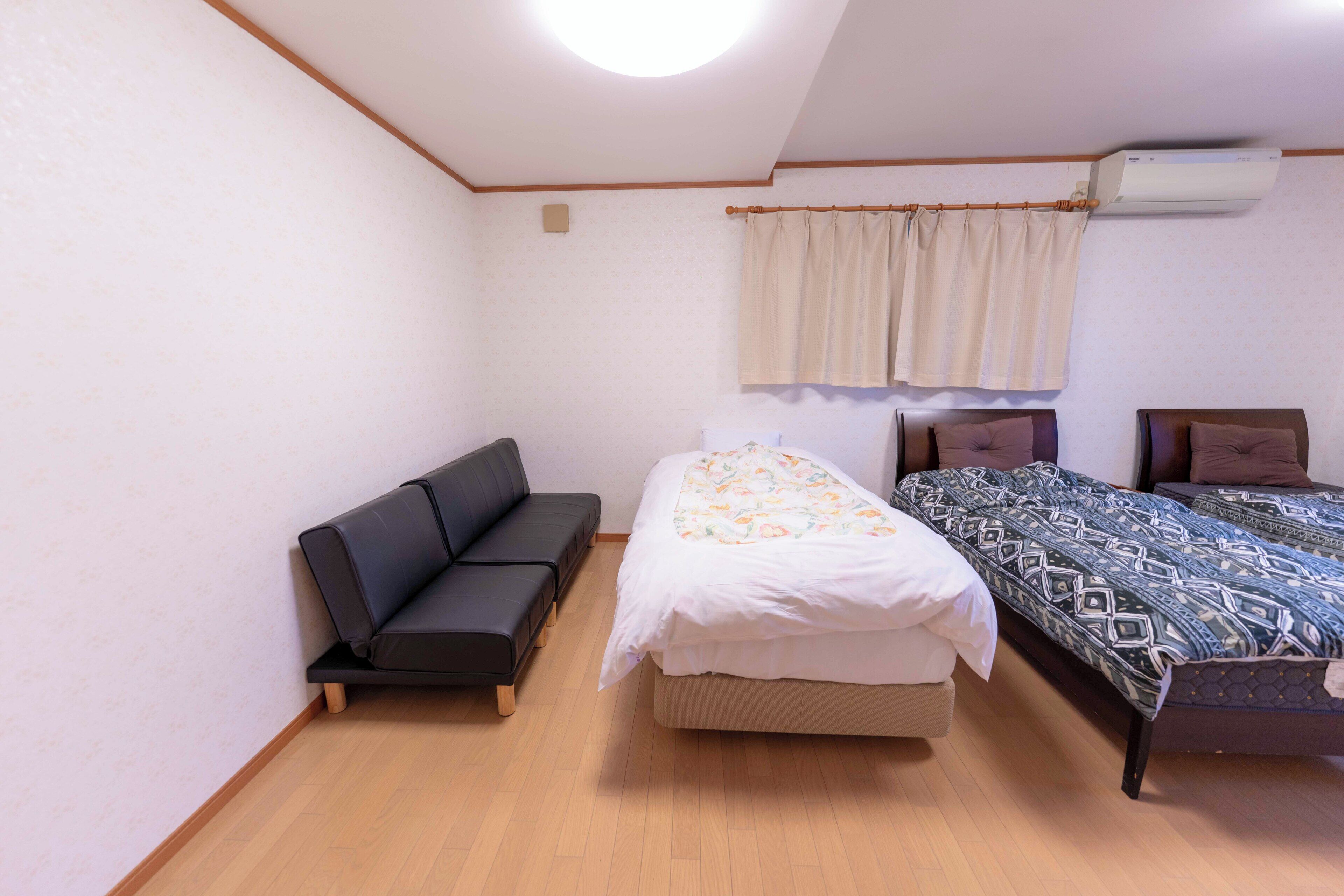 A room with a black sofa, a bed with a patterned bedspread, and a second bed with a geometric patterned bedspread.
