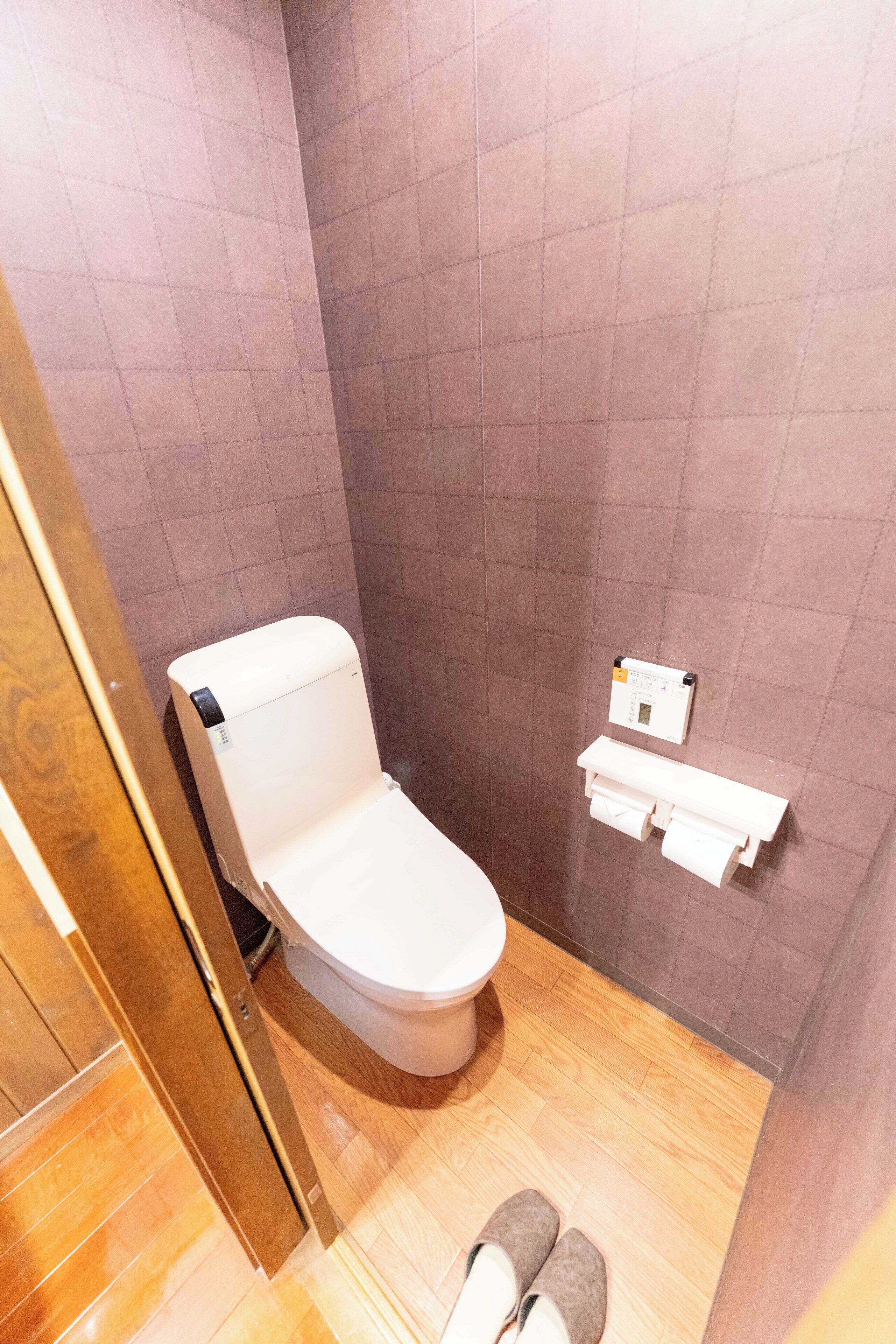 Ein kleines, kompaktes Badezimmer mit Toilette, Holzboden und einem an der Wand befestigten Toilettenpapierhalter.