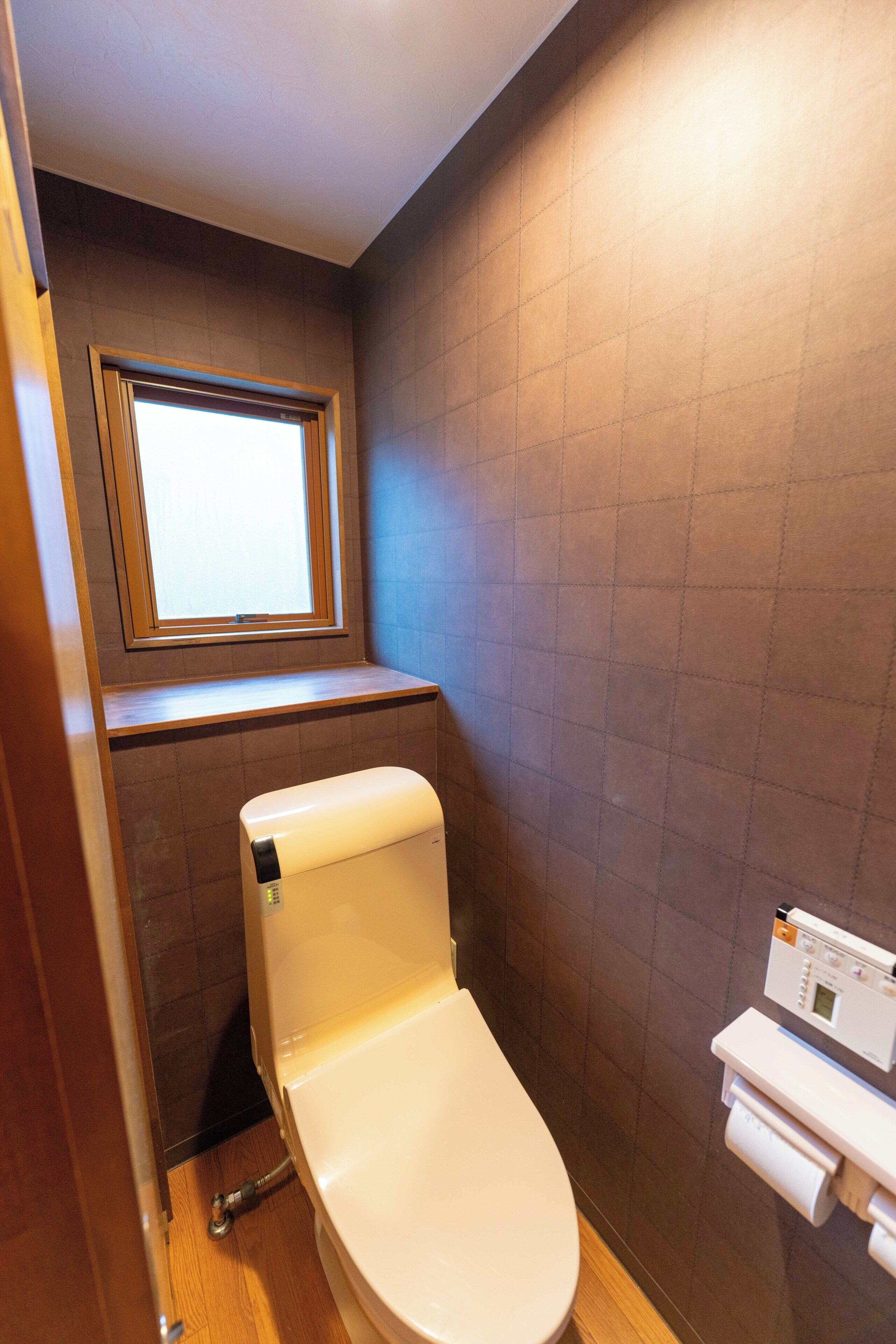 A small bathroom with a toilet, a window, and a wall-mounted toilet paper dispenser.
