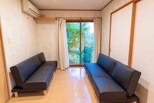 Una habitación con dos sofás negros, suelo de madera, una ventana con cortinas y un equipo de aire acondicionado.