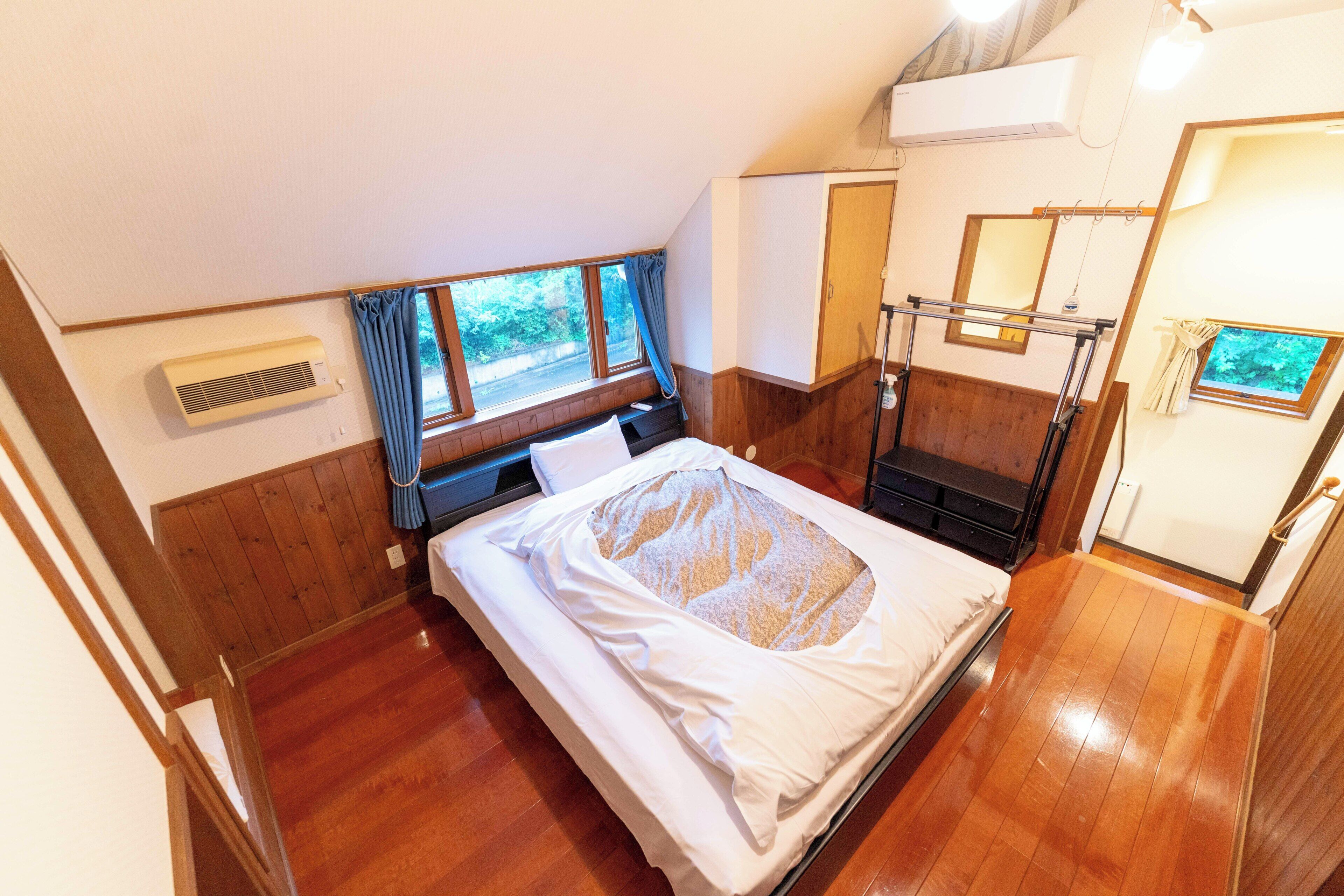 Une chambre à coucher avec un lit, une fenêtre, un appareil de climatisation, un plancher en bois et une porte.