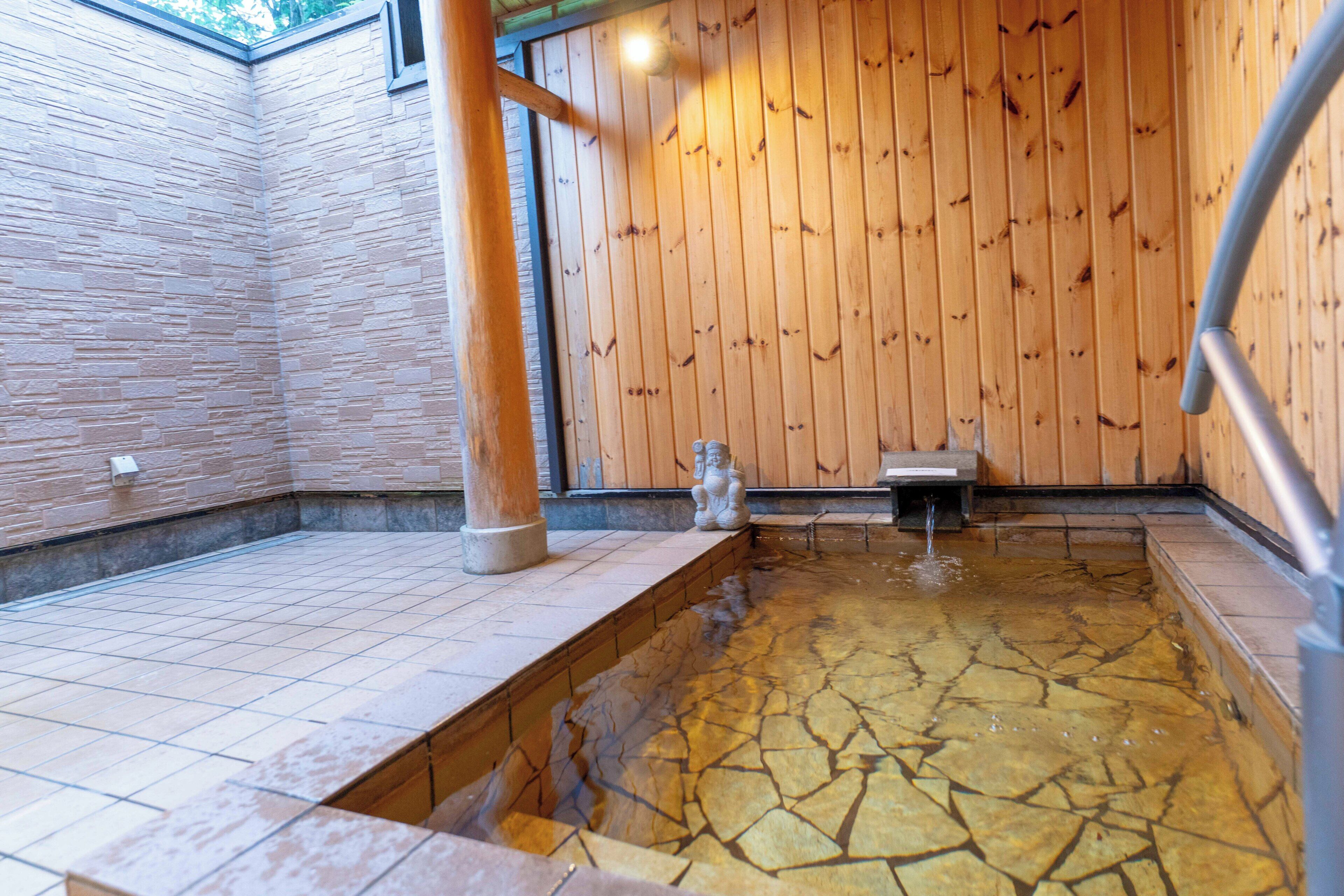 A traditional Japanese onsen with a stone bath, wooden walls, and a stone floor.