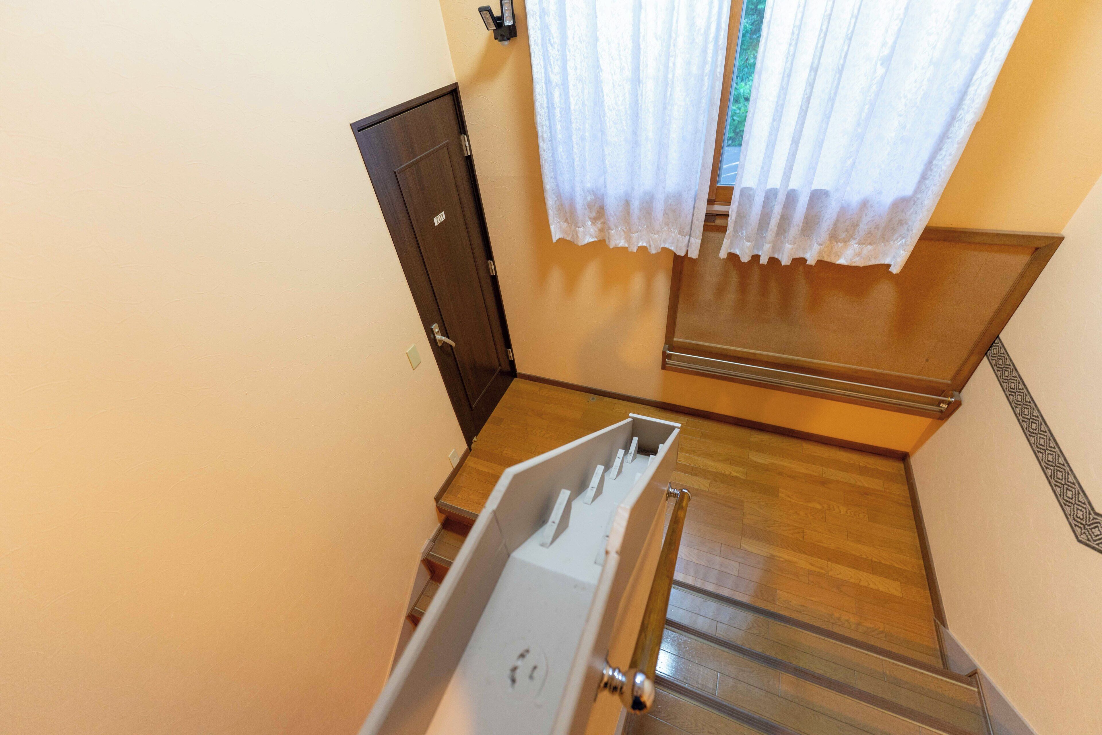 A narrow stairway with a wooden handrail, a white wall, and a door with a number plate.