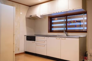 A kitchen with white cabinets, a dishwasher, and a window with blinds. - TOMONOWA (Bandai)
