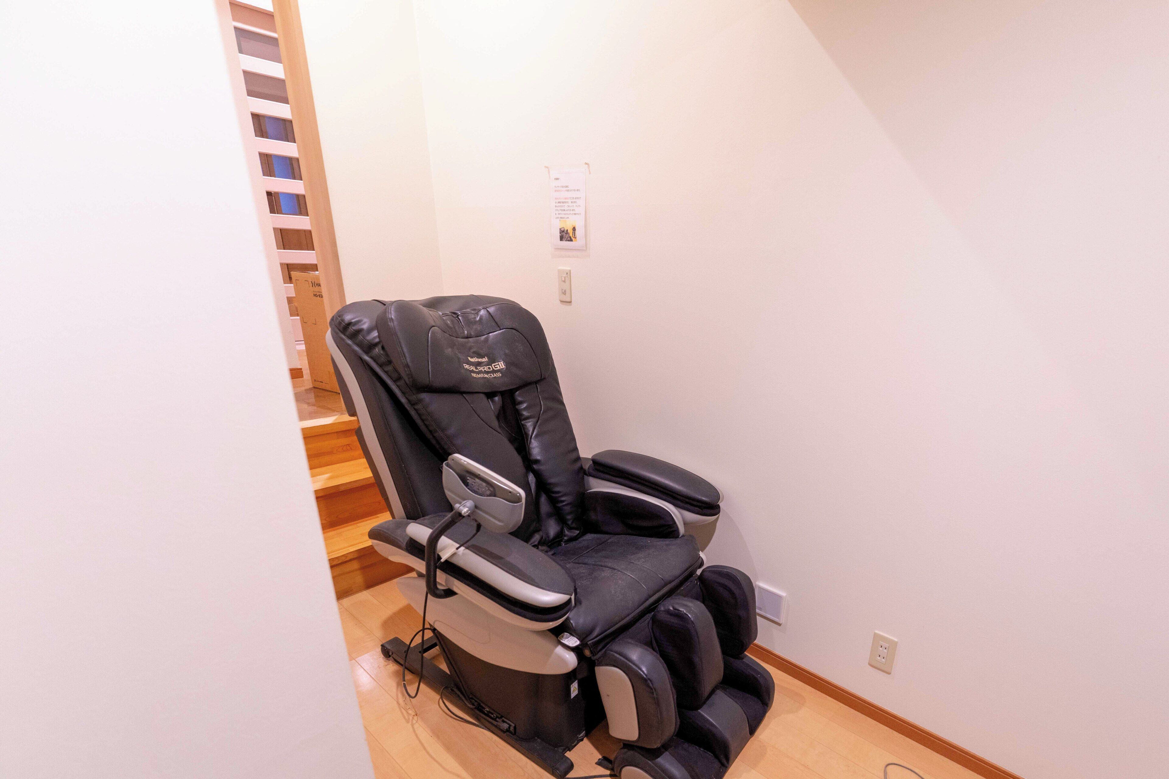 A massage chair in a room with a wooden staircase and a white wall.