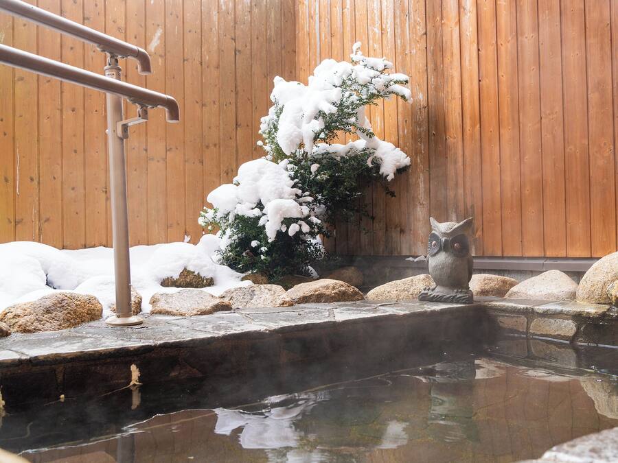 A hot spring area with a wooden wall, rocks, and a stone ledge.