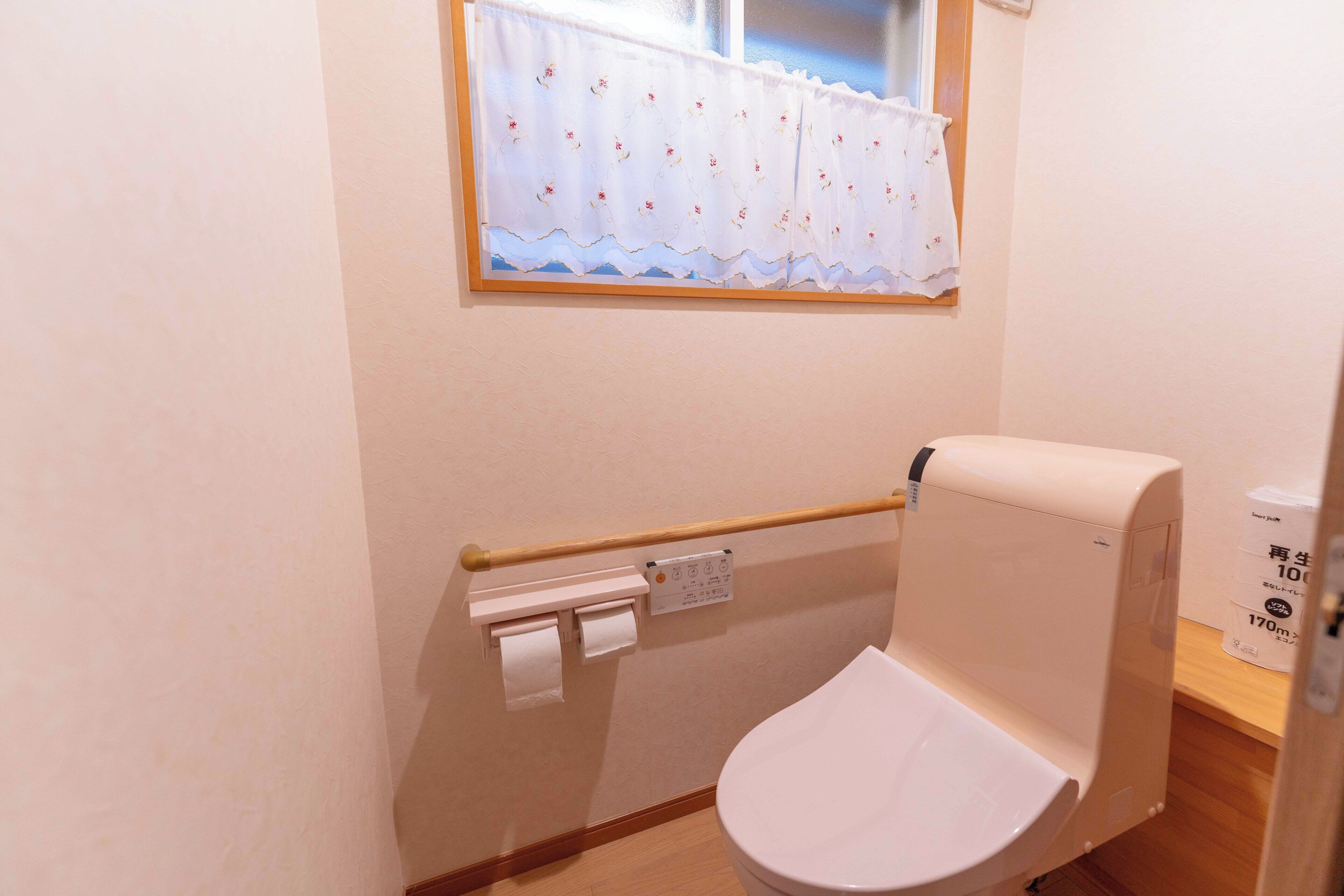 A small bathroom with a toilet, a toilet paper holder, and a window with a floral curtain.