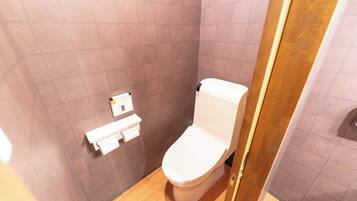 A small bathroom with a toilet, a paper towel dispenser, and a wooden floor.