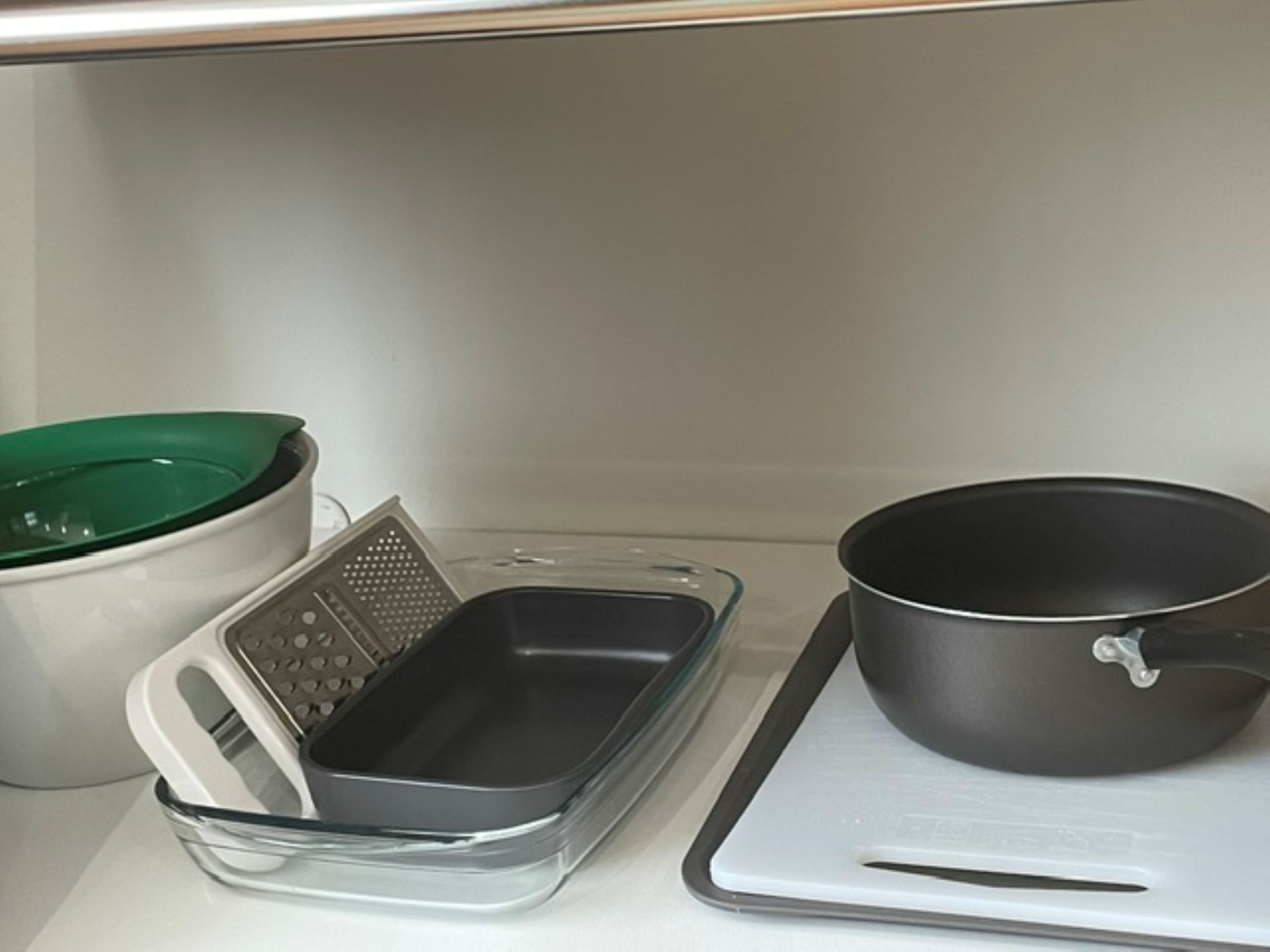 Une cuisine avec un plan de travail blanc, un pot vert et blanc, une râpe et une poêle noire.