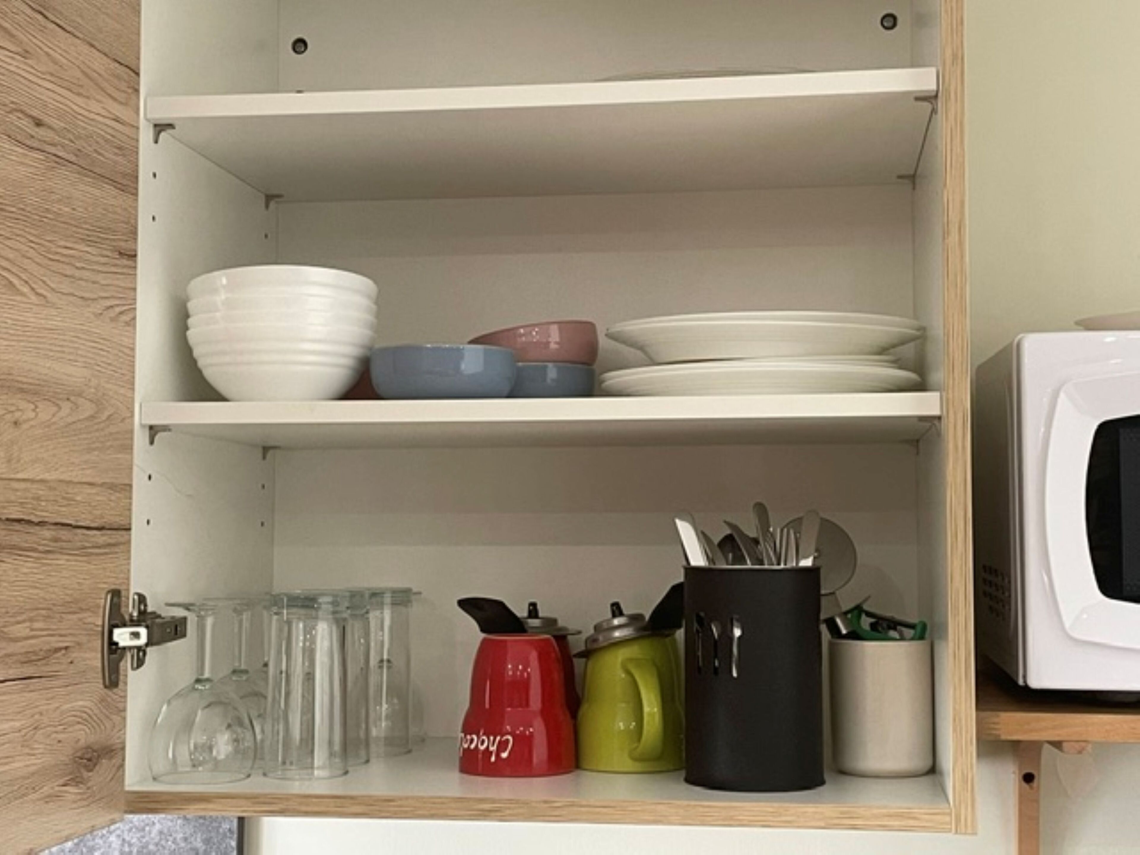 Eine Küchenschrank mit Regalen, voll mit Schüsseln, Tellern, einer Mikrowelle und verschiedenen Küchenutensilien.