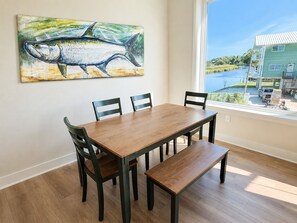 Spiseområde med et træbord og stole, en bænk og et stort maleri af en fisk på væggen.
