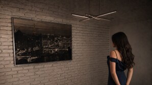Eine Frau in einem dunklen Kleid steht vor einem großen schwarz-weißen Stadtbildes an einer Ziegelwand.