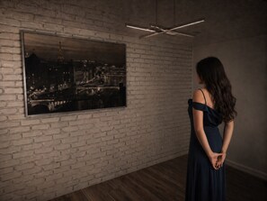 Eine Frau in einem dunklen Kleid steht vor einem großen schwarz-weißen Stadtbildes an einer Ziegelwand.