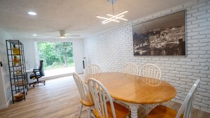 Ein Essbereich mit Backsteinwand, einem runden Holztisch, weißen Stühlen und einem Deckenventilator.