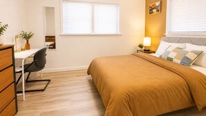 Ein Schlafzimmer mit einem Bett, einem Schreibtisch, einem Stuhl, einem Nachttisch und einem Fenster mit Jalousien.