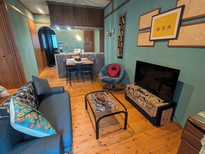 Ein Wohnzimmer mit Sofa, Sessel, Couchtisch und Kamin. Im Hintergrund befindet sich ein Essbereich mit Tisch und Stühlen.