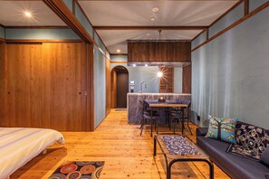Ein modernes Interieur mit Holzboden, einer Couch mit gemusterten Kissen, einem Essbereich mit Tisch und Stühlen sowie einer Küche mit Marmorarbeitsplatte.