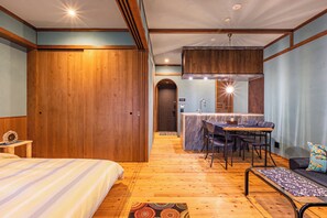 Ein Hotelzimmer mit Holzboden, einem Bett, einem Schreibtisch mit Stühlen, einer kleinen Küchenzeile und einem Badezimmer.