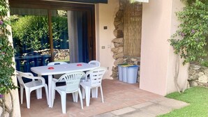Een terras buiten met een tafel, stoelen, een stenen muur en een overdekt gedeelte.
