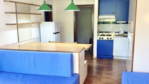 Een kleine keuken met een fornuis, koelkast en hangende groene hanglampen.