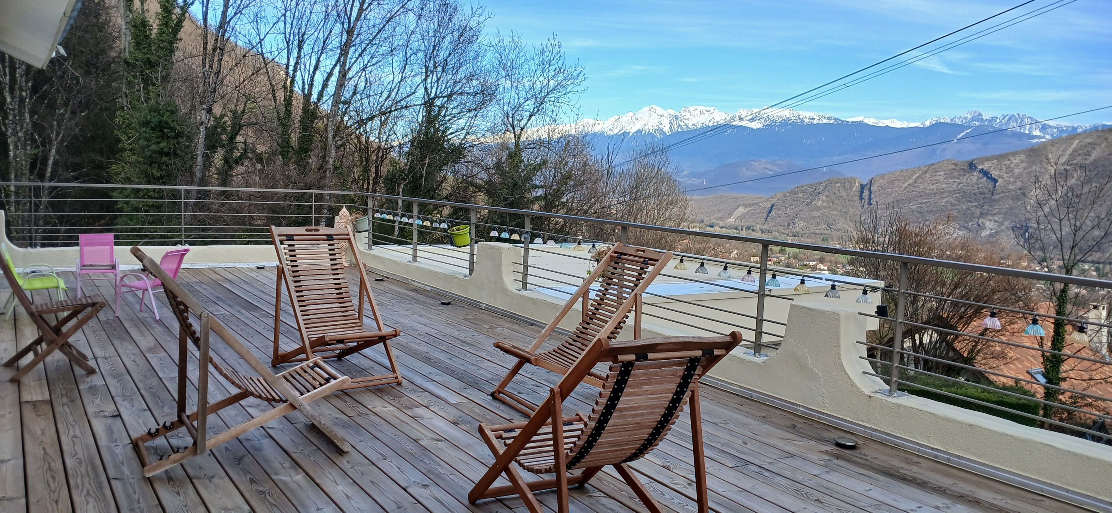 Eine Holzterrasse mit Liegestühlen mit Blick auf eine gebirgige Landschaft.