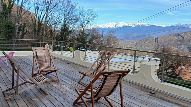 Eine Holzterrasse mit Liegestühlen mit Blick auf eine gebirgige Landschaft.