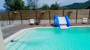 Ein Swimmingpool mit einer blauen aufblasbaren Rutsche, umgeben von einer Holzterrasse und Stühlen.