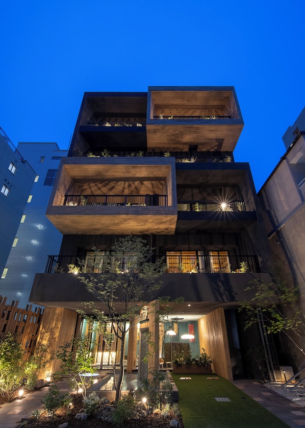 A multi-story building with balconies, a garden area, and a pathway leading to the entrance. - Stylish Apartment with Balcony, Walk to Dotonbori, Shinsaibashi, & Kuromon Mkt (大阪市)