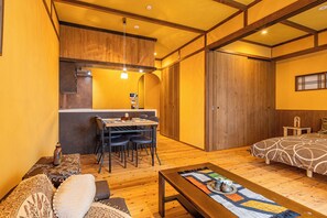 A compact room with a wooden dining table, chairs, a sofa, and a bed with a patterned bedspread. - Stylish Apartment with Balcony, Walk to Dotonbori, Shinsaibashi, & Kuromon Mkt (大阪市)