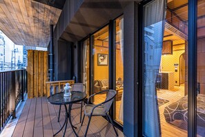 A wooden deck with a table and chairs, a view into a room with a bed and a sofa, and a glass door leading to an outdoor area. - Stylish Apartment with Balcony, Walk to Dotonbori, Shinsaibashi, & Kuromon Mkt (大阪市)