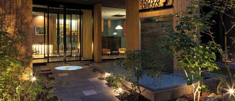A hotel entrance with a stone pathway, indoor seating area, and a sign above the door.