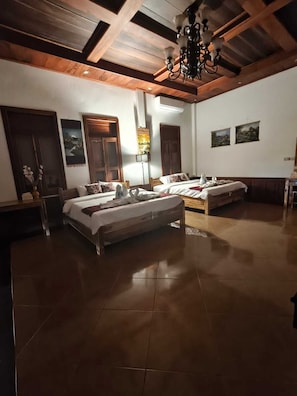 Une chambre d’hôtel avec deux lits, des poutres en bois au plafond, un lustre et des œuvres d’art accrochées aux murs.