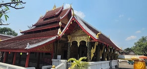 A traditional multi-tiered temple with ornate golden decorations and a red roof. - Loaviengluabgprabang guesthouse (Luang Prabang)
