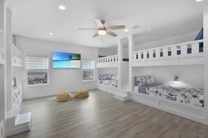 Une chambre avec des lits superposés, un ventilateur de plafond, une télévision et une fenêtre avec des stores.