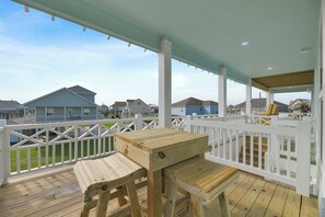 Une terrasse en bois avec une table et des chaises, des rampes blanches et des maisons en arrière-plan.