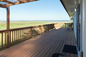 Eine Holzterrasse mit Geländer, Blick auf ein grünes Feld und einen klaren Himmel.