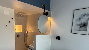 Ein modernes Schlafzimmer mit Bett, Nachttisch, Spiegel und Duschbereich.
