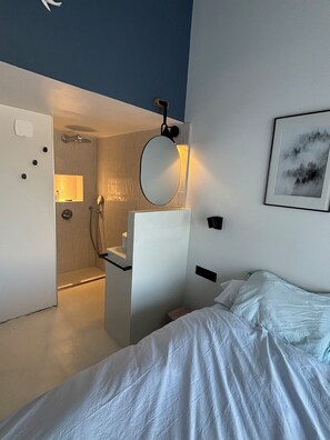A modern bedroom with a bed, a bedside table, a mirror, and a shower area. - Very pleasant house with swimming pool, garden, air conditioning - 10 min from the beaches (Pérols)