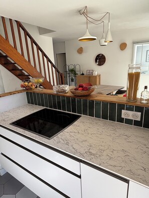 A kitchen with a built-in stove, wooden staircase, and pendant lighting. - Very pleasant house with swimming pool, garden, air conditioning - 10 min from the beaches (Pérols)