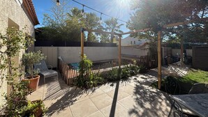 Eine Terrasse mit einer Pergola, Sitzgelegenheiten im Freien und Topfpflanzen.