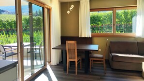 A room with a dining table, chairs, a sofa, and large windows offering a view of greenery. - Highlight Apartments: Ap. Harmony with garden access, loggia and Mobil Card incl. (Sankt Pauls)