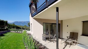 A modern outdoor patio with a table and chairs, a glass door leading inside, and a view of mountains in the background. - Highlight Apartments: Ap. Harmony with garden access, loggia and Mobil Card incl. (Sankt Pauls)